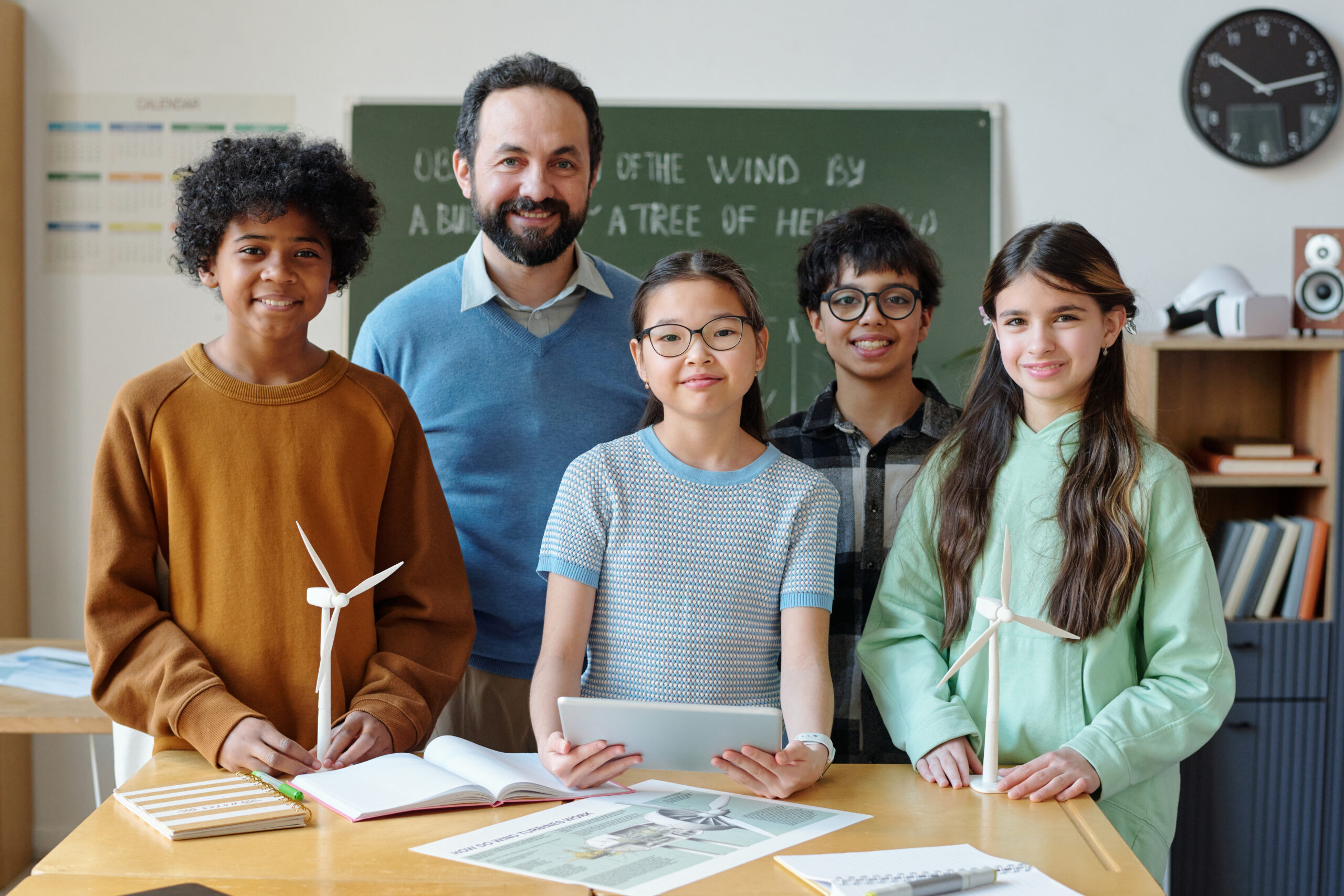 Teacher and students gathered around a classroom table with a tablet and a model wind turbine