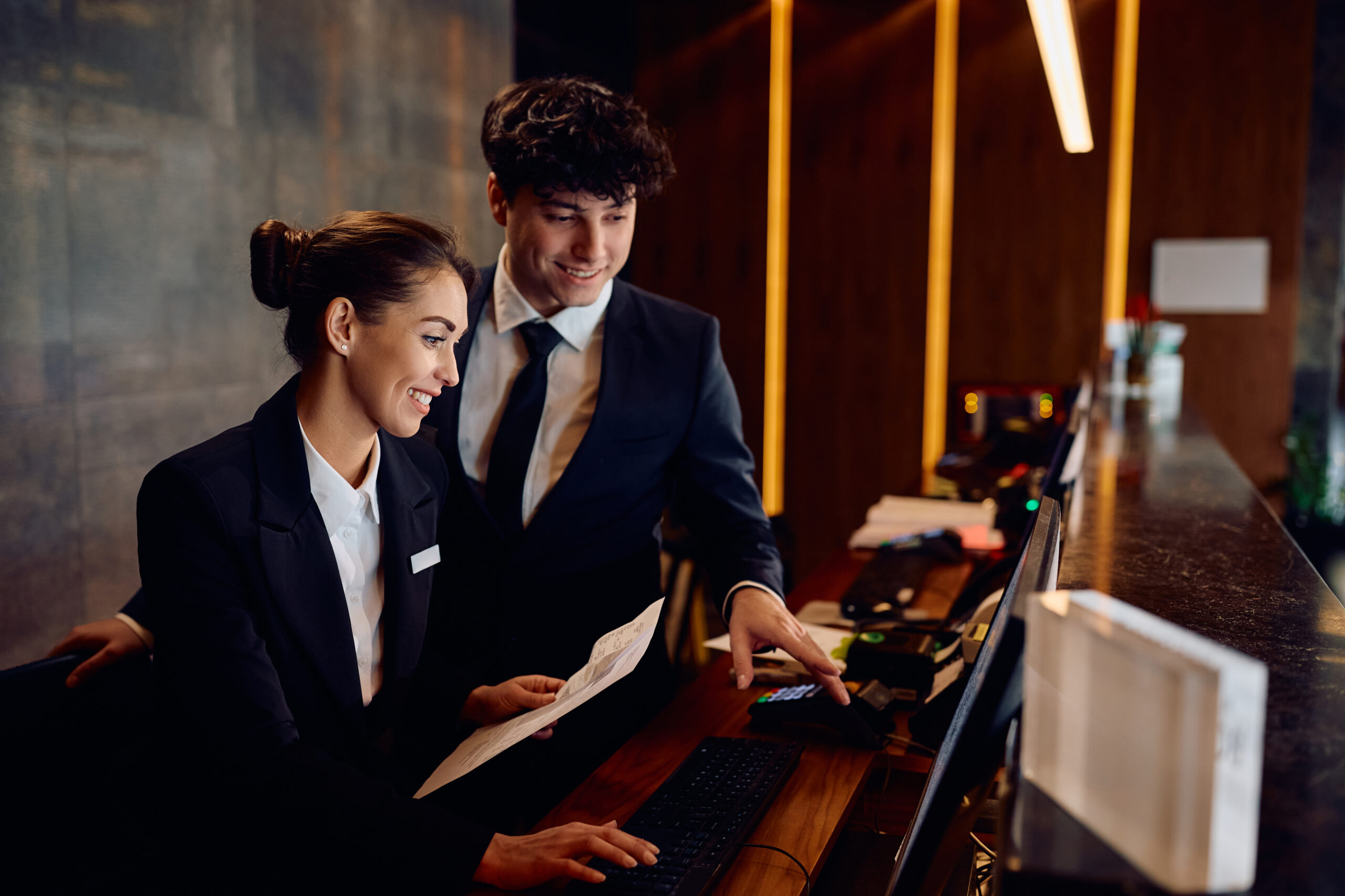 Hotel reception colleagues reviewing a booking on a computer at the front desk