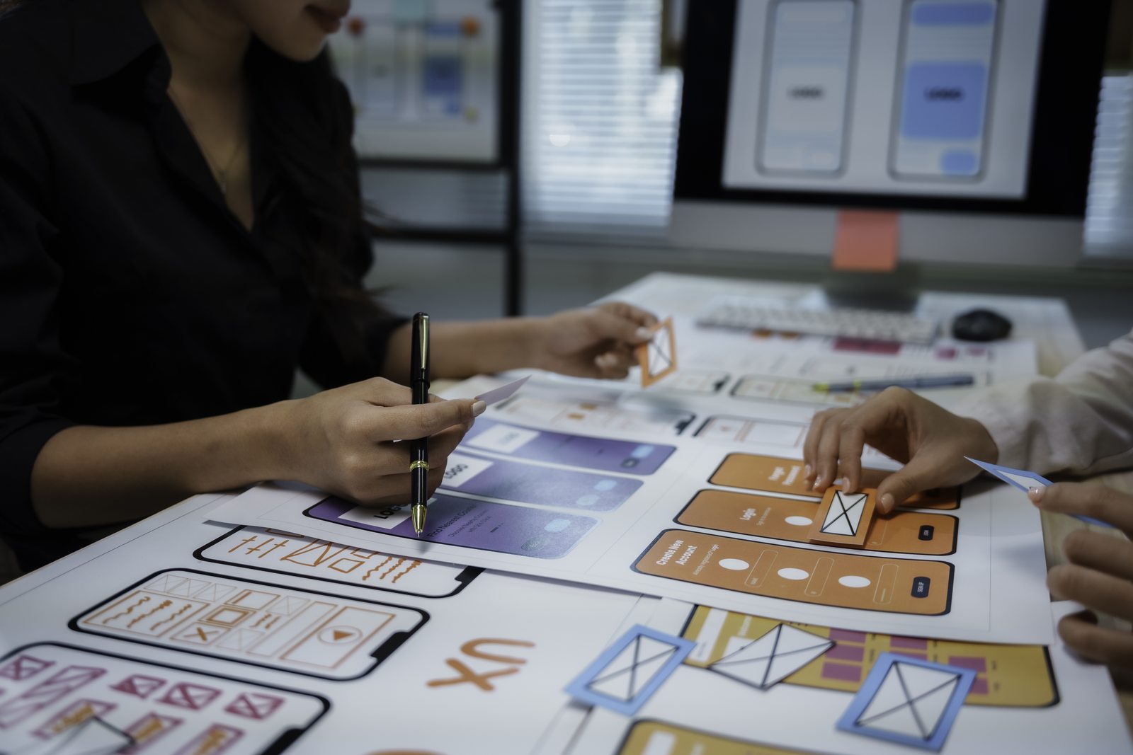 Designers reviewing paper interface layouts beside a computer