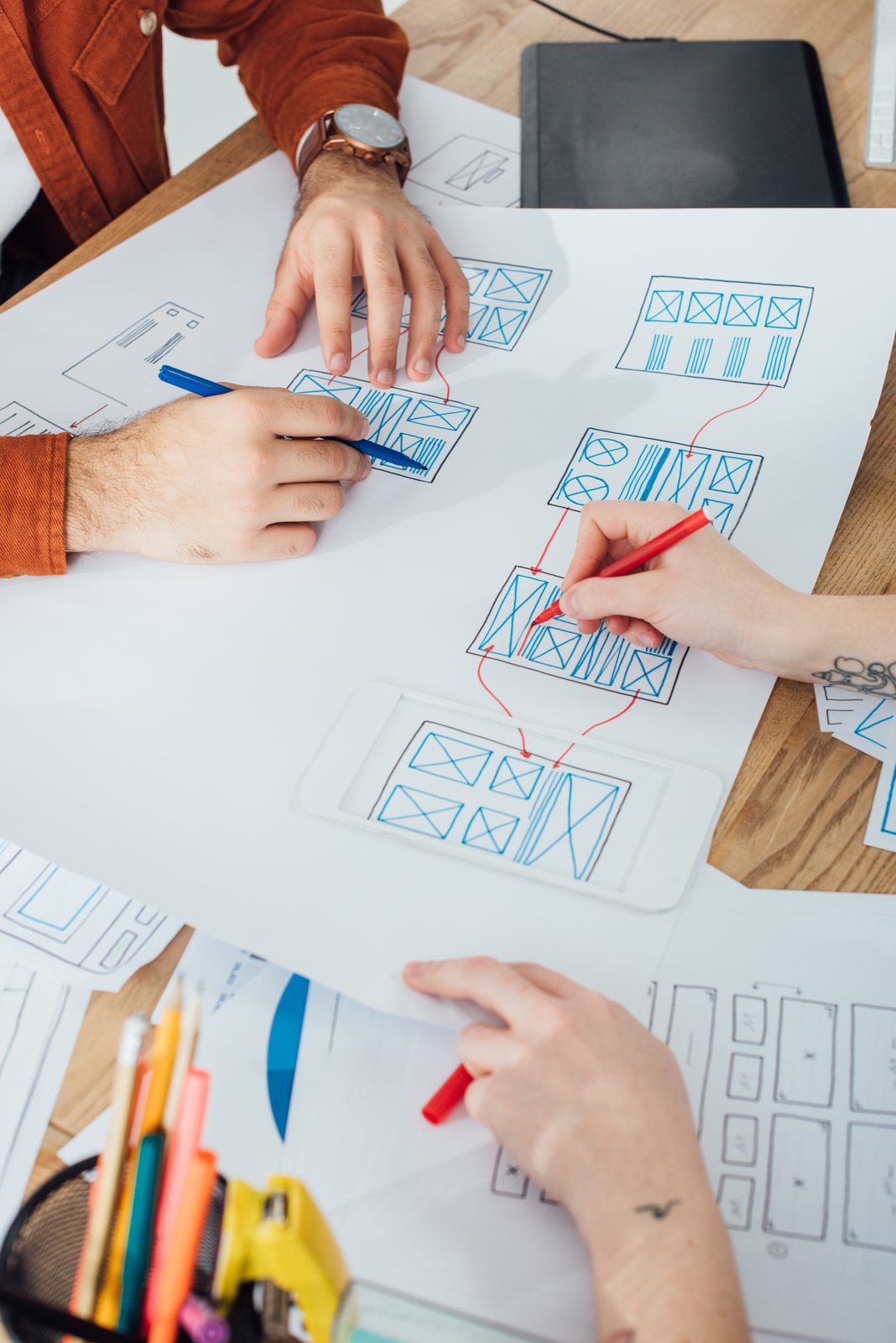 Hands sketching interface wireframes together around a table