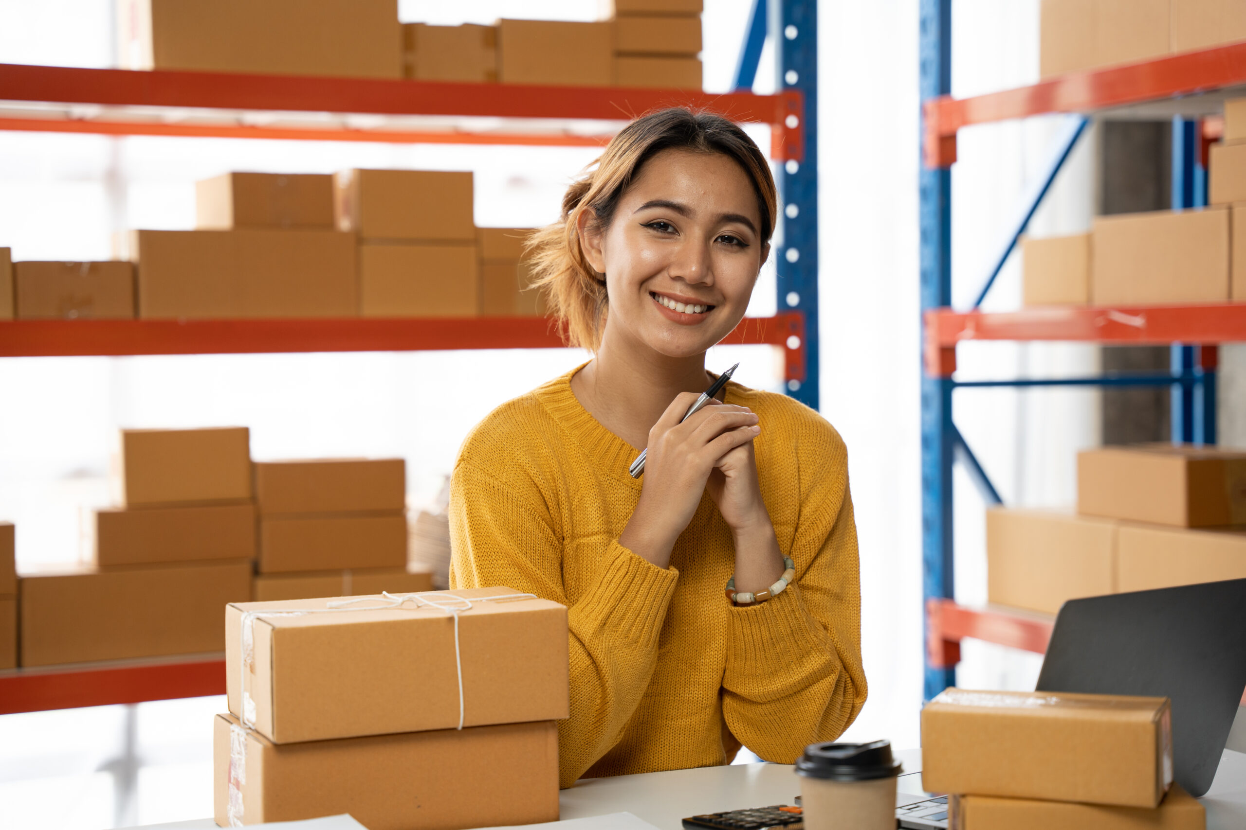 Retail business owner at a packing desk with parcels and a laptop in a warehouse