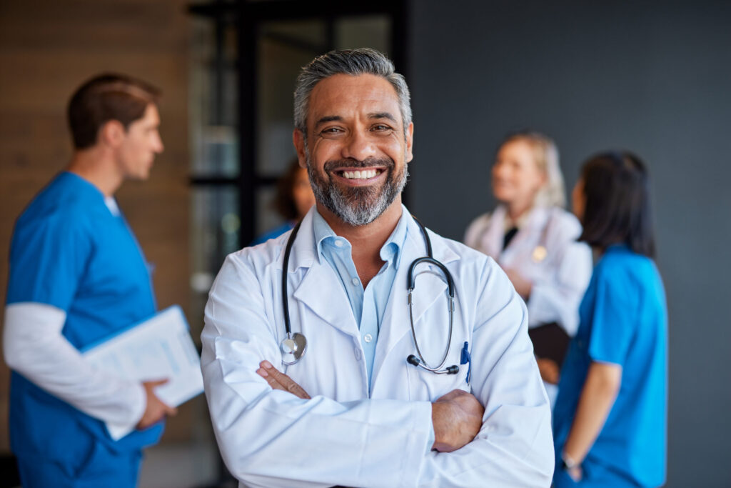 Doctor smiling in a medical office with colleagues in the background; illustrative photograph