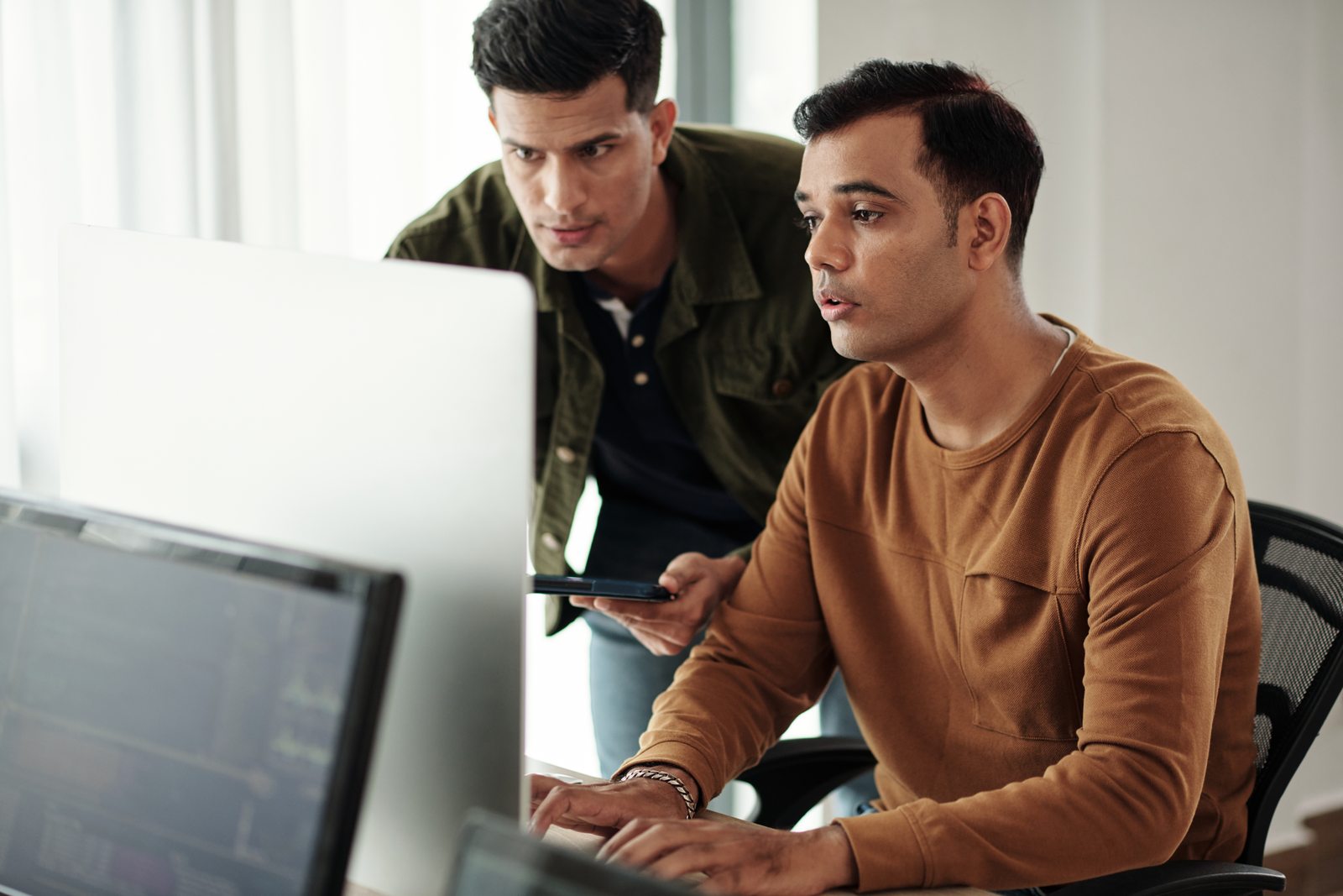 Two colleagues reviewing software on desktop computers; illustrative photography